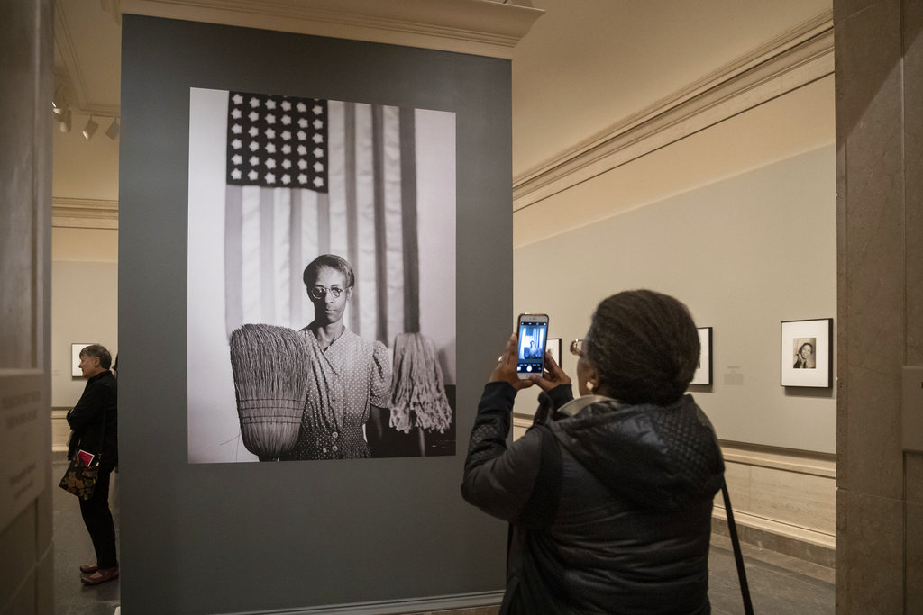 Jessica White, from San Francisco, takes a snapshot using her phone as she enters an exhibition at the National Gallery of Art of the work of photojournalist, musician, writer and film director Gordon Parks, in Washington, Tuesday, Oct. 30, 2018. Her father, the African-American artist Charles White, was a friend of Parks, as well as the subject of one of the photos in the exhibit. Shown is Parks's iconic 1942 photograph called American Gothic and portrays Ella Watson who worked cleaning the offices of the Farm Security Administration in Washington. (AP Photo/J. Scott Applewhite)