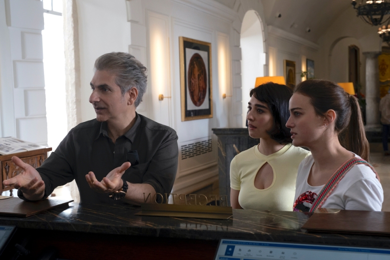 A middle-aged man and two young women at a hotel reception counter; still from The White Lotus Season 2.