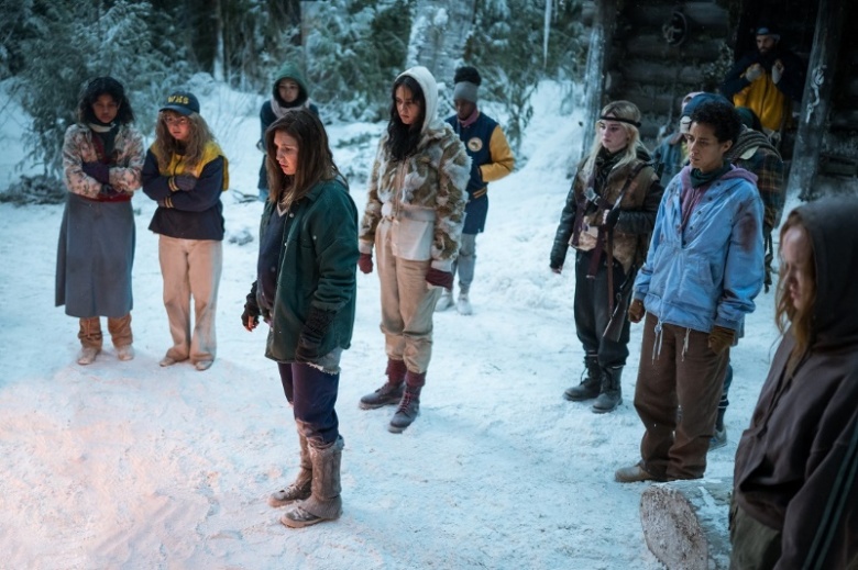 A group of teenage girls stand around in a snowy forest; still from Yellowjackets Season 2.