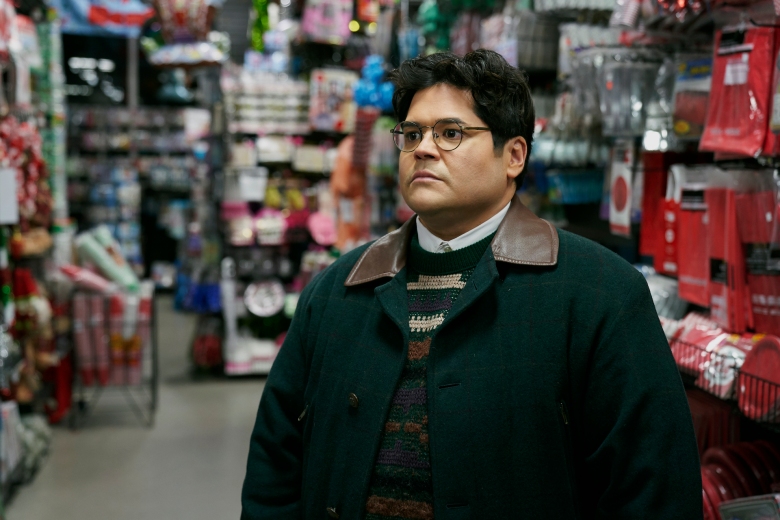 A young man with glasses in a striped sweater and dark green coat looking somber in a store; still from What We Do in the Shadows